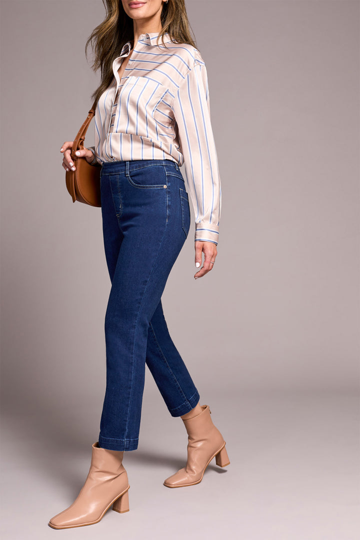 Woman wearing a striped shirt, blue jeans, and beige boots with a brown handbag on a gray background