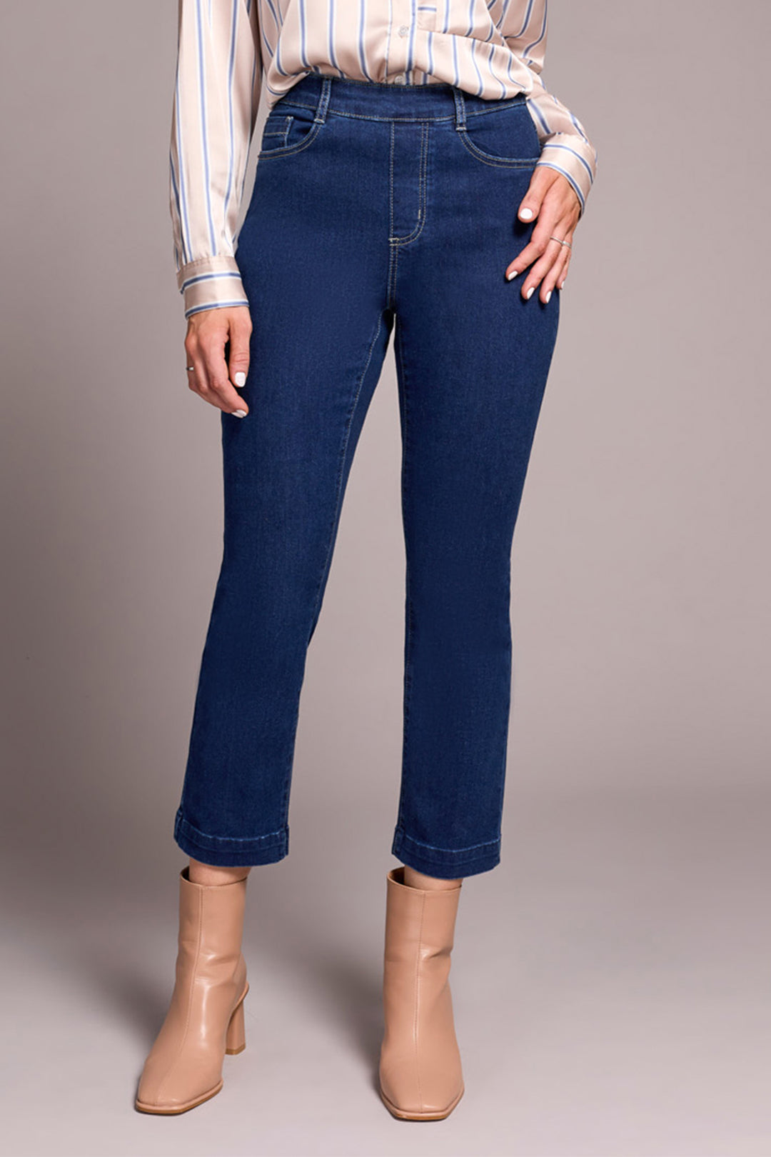 Person wearing blue jeans and beige boots on a plain background