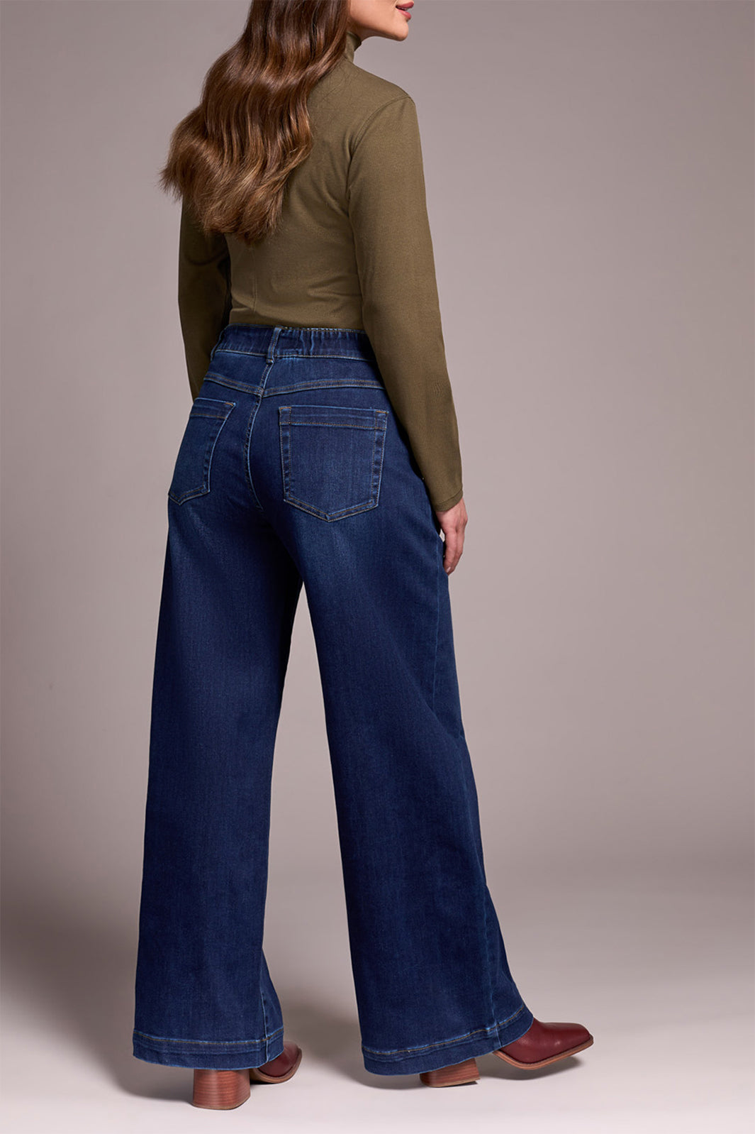 Person wearing a green top and blue jeans against a plain background
