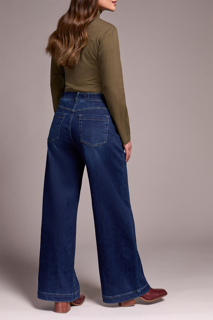Person wearing a green top and blue jeans against a plain background