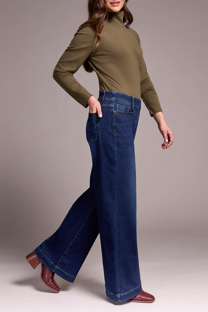 Woman wearing a green long-sleeve top and blue jeans on a gray background