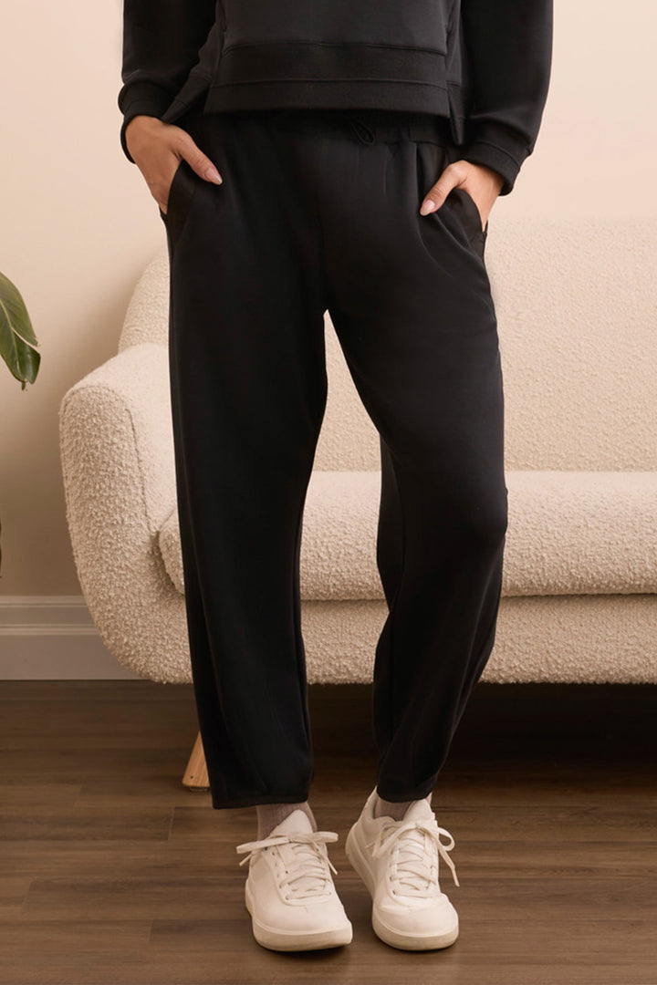 Person wearing black jogger pants and white sneakers standing in a room with a beige sofa.