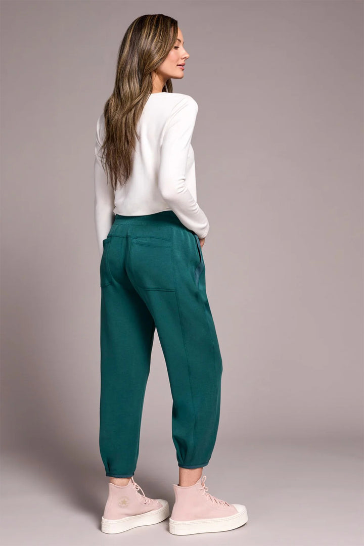 Woman wearing teal pants and a white top against a plain background