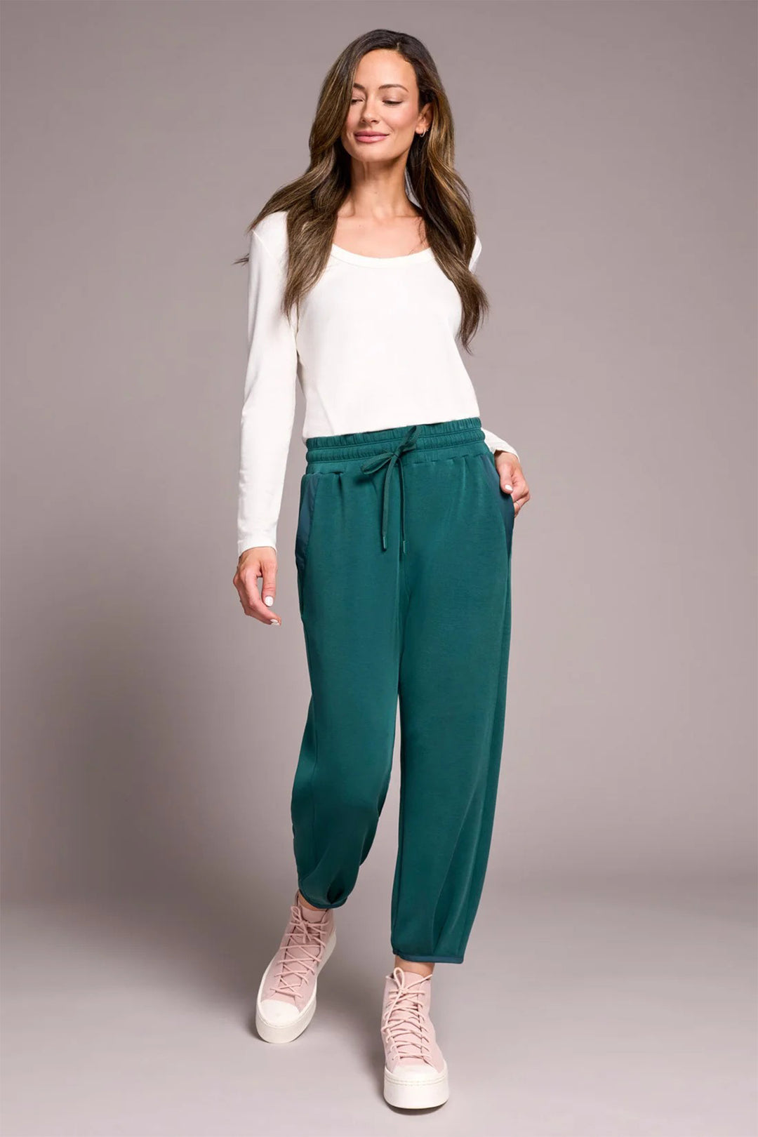 Woman wearing a white top and green pants against a plain background