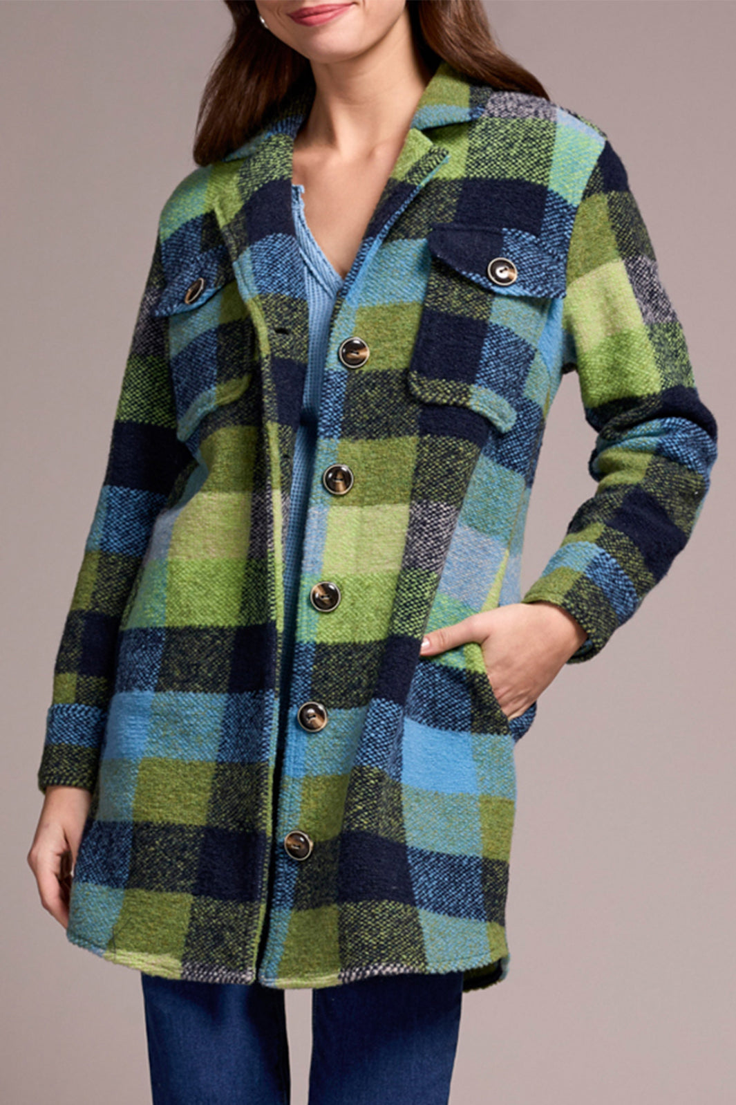 Woman wearing a plaid coat with green, blue, and black pattern on a neutral background