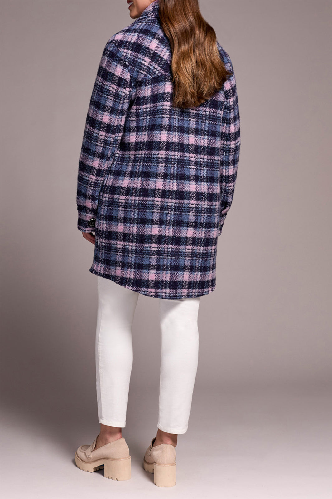 Person wearing a plaid coat and white pants against a neutral background