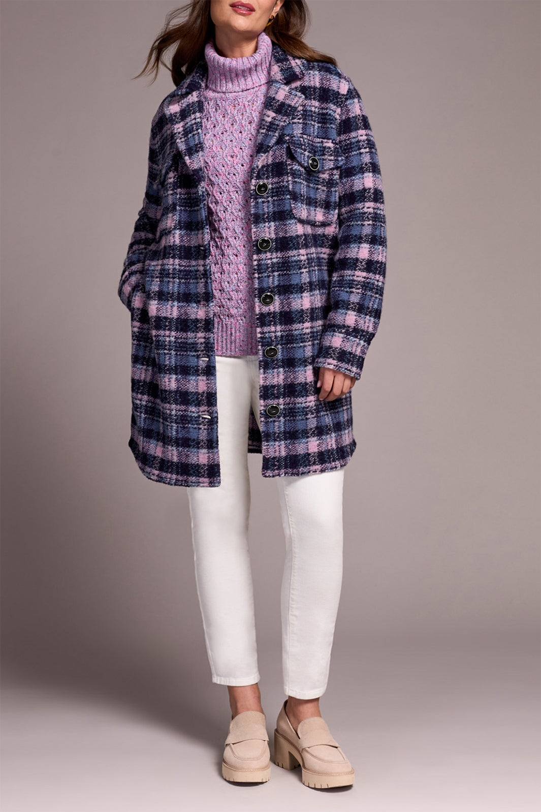 Person wearing a plaid coat over a pink sweater with white pants on a plain background