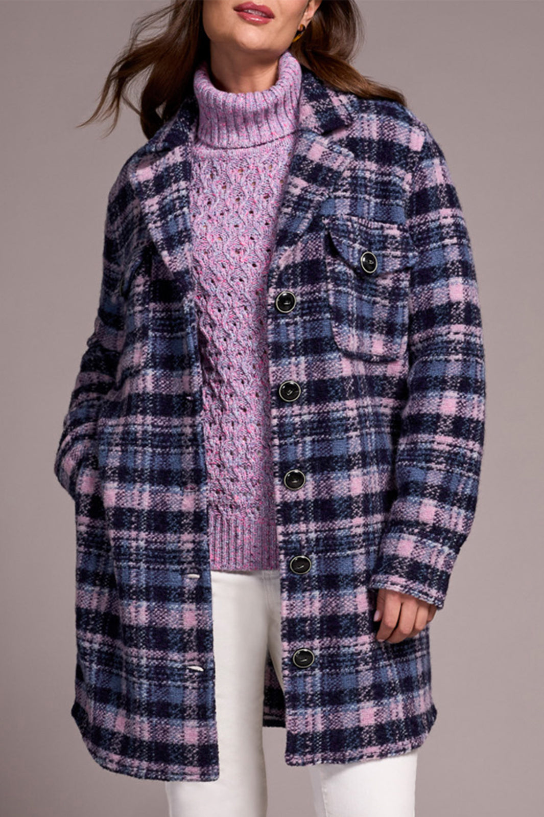 Person wearing a plaid coat over a pink sweater on a gray background