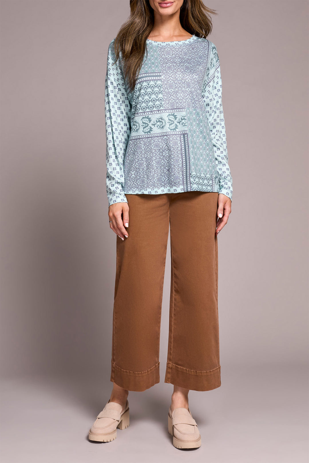 Woman wearing a patterned blue top and brown pants on a plain background