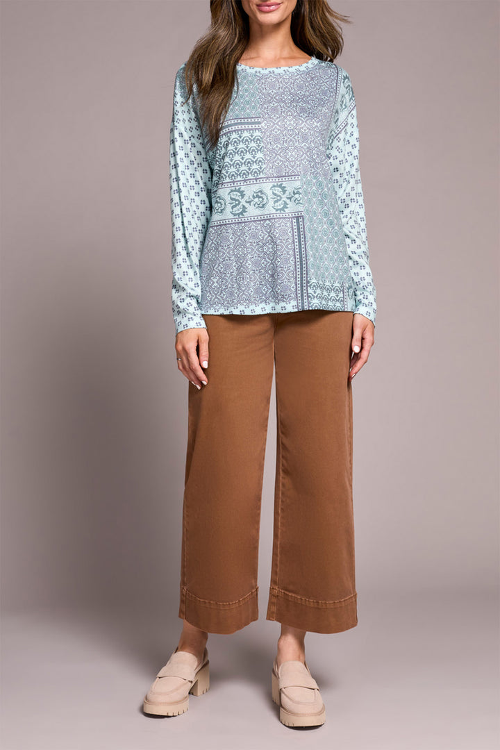 Woman wearing a patterned blue top and brown pants on a plain background