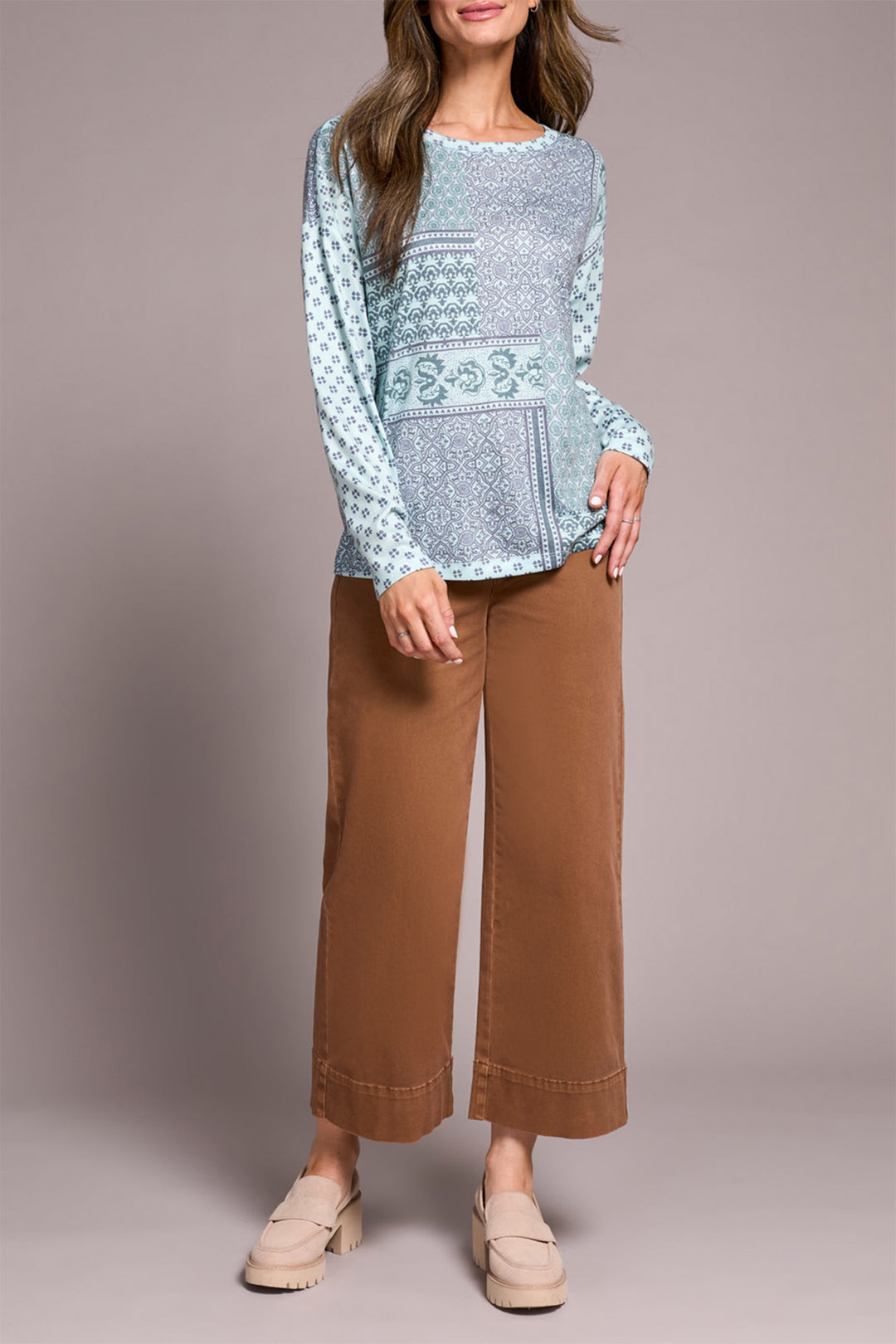 Woman wearing a light blue patterned top and brown pants against a plain background