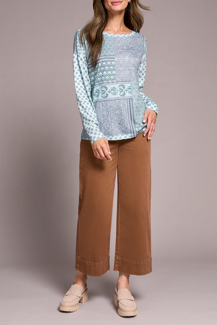 Woman wearing a light blue patterned top and brown pants against a plain background