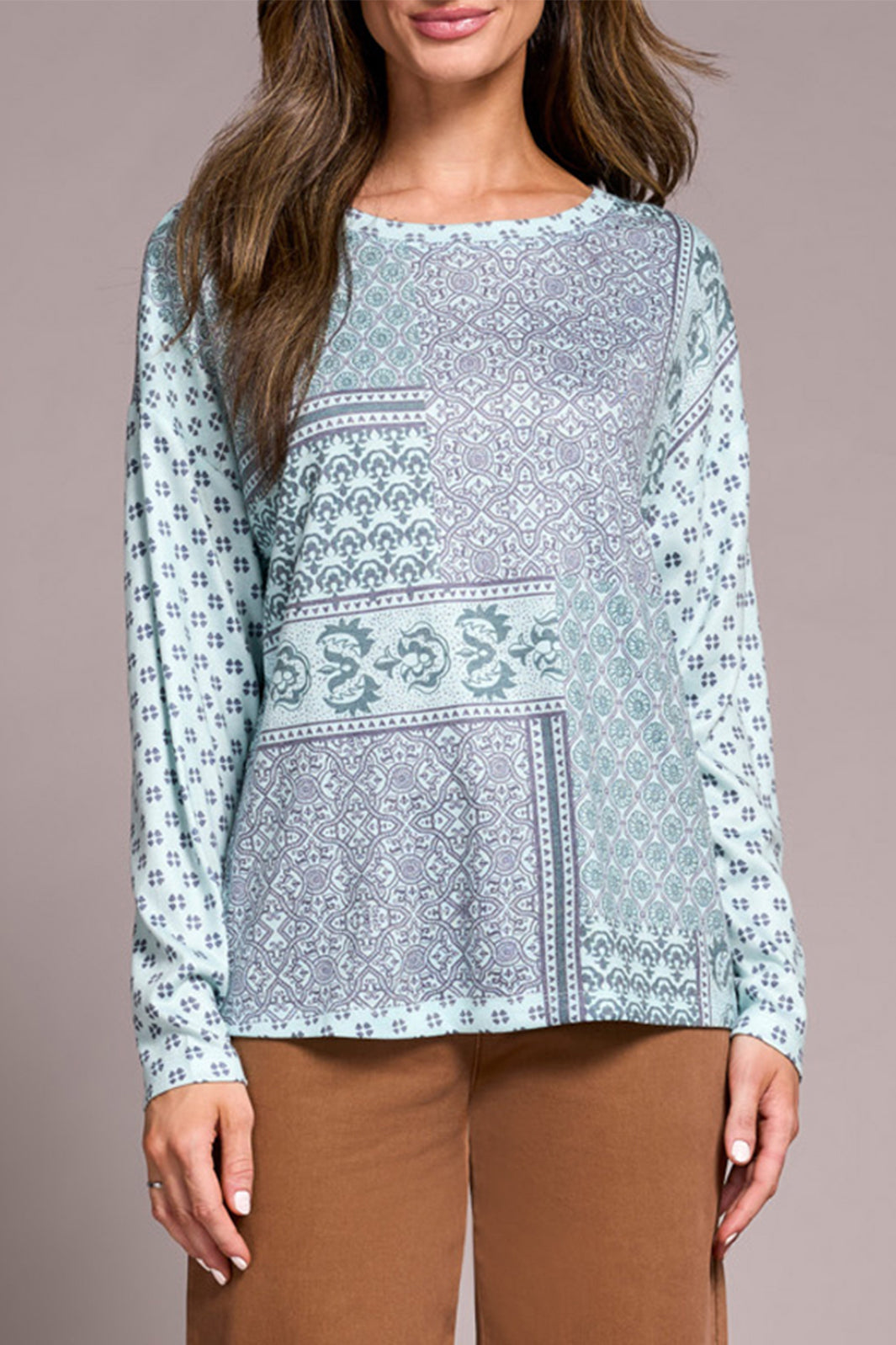 Woman wearing a light blue patterned top with brown pants on a beige background