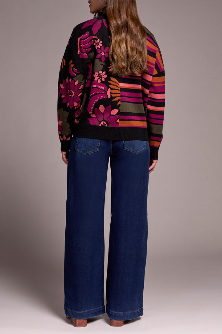 Person wearing a colorful patterned sweater and blue jeans on a plain background