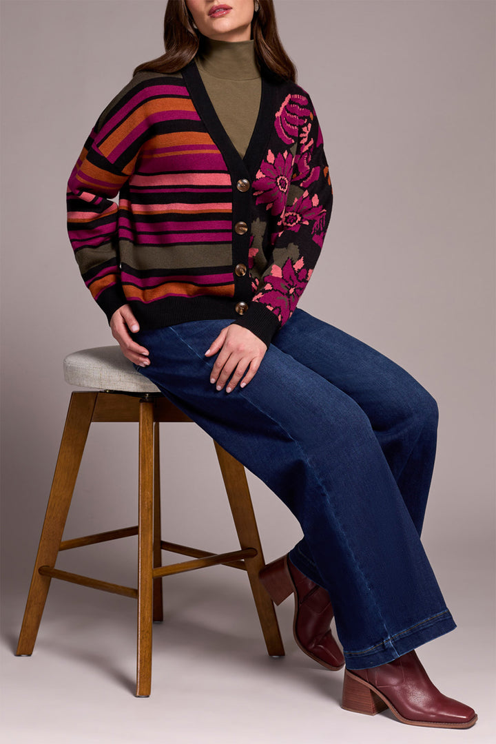 Woman sitting on a stool wearing a colorful cardigan with floral patterns and striped design.