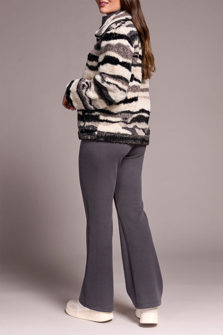 Person wearing a patterned jacket and gray pants on a plain background