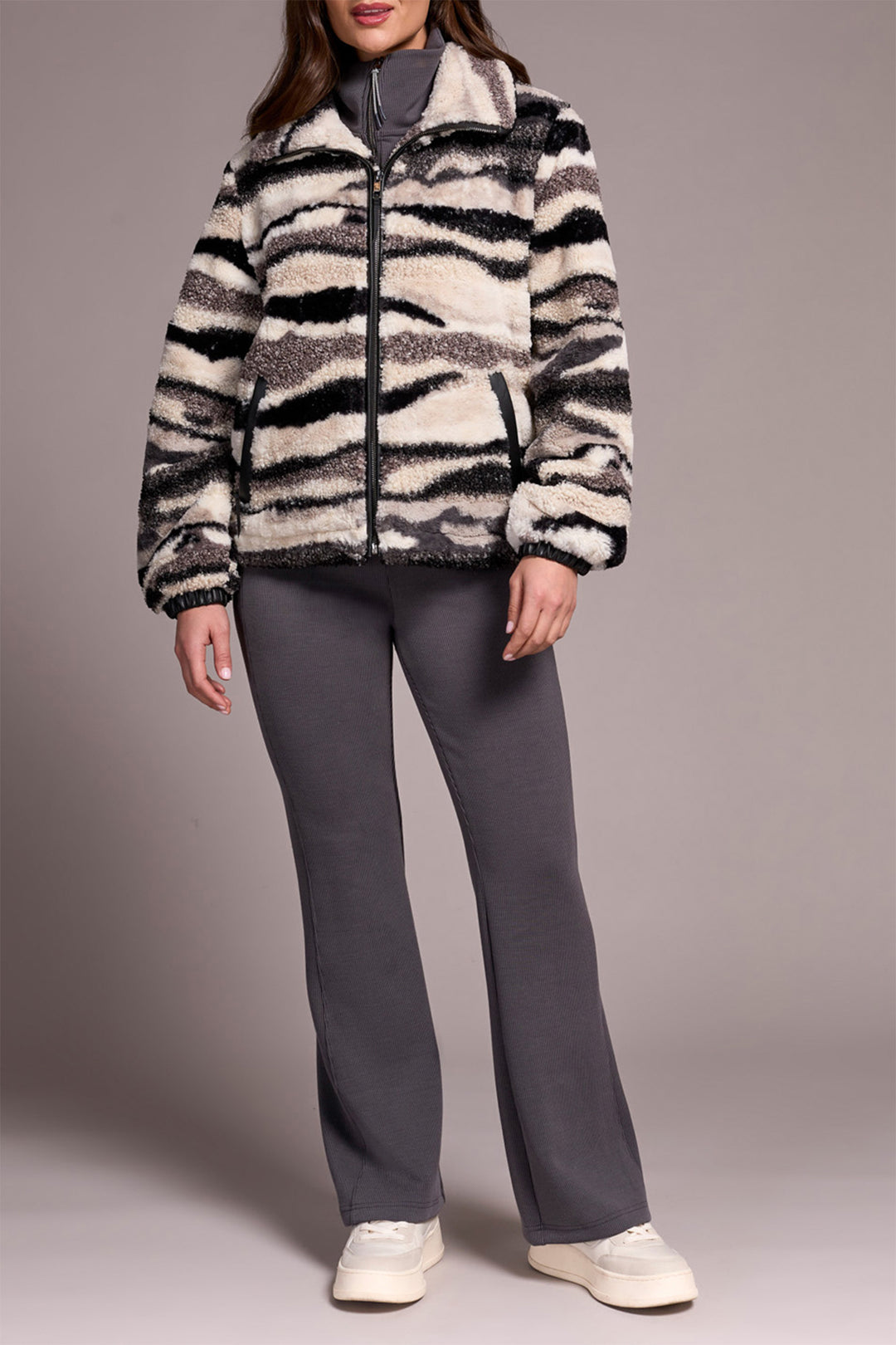 Person wearing a zebra-striped jacket and gray pants on a plain background