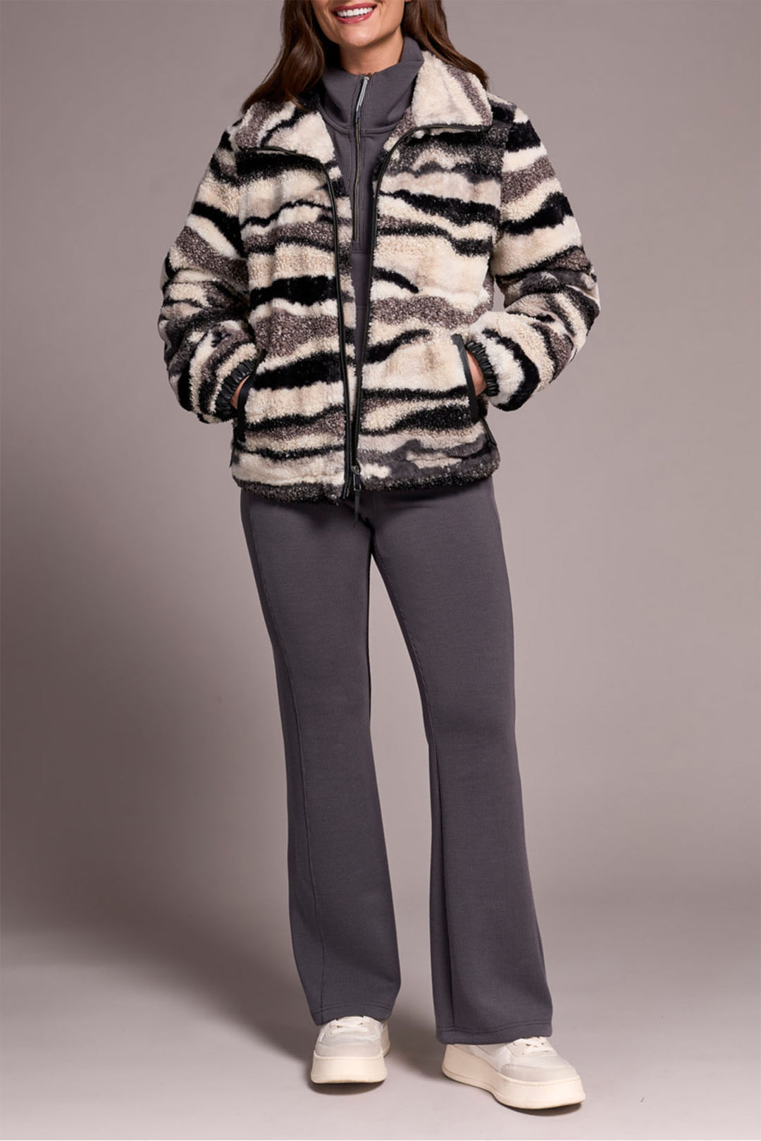 Person wearing a zebra-striped jacket and gray pants on a plain background