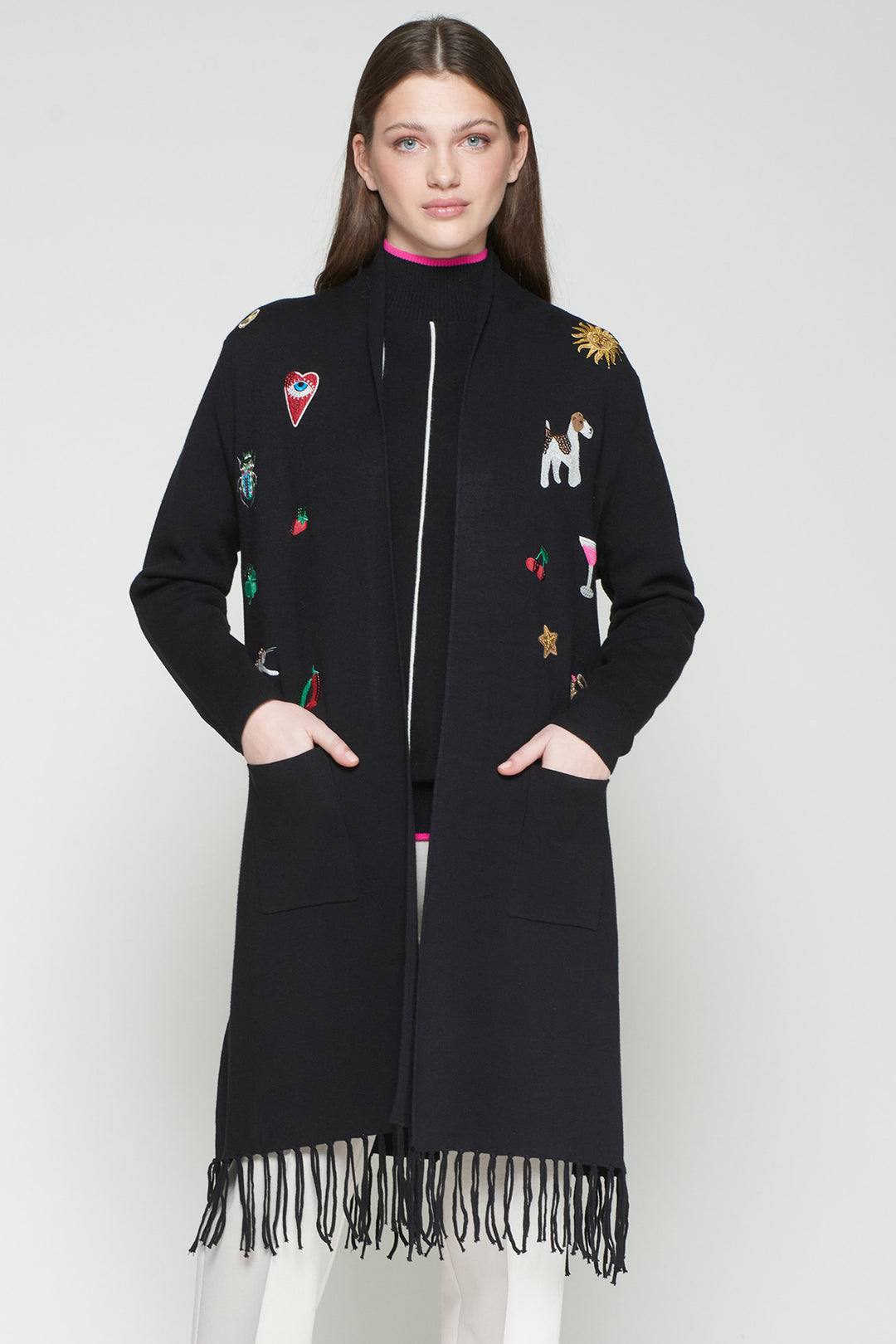 Woman wearing a black coat with colorful embroidery and fringes on a white background