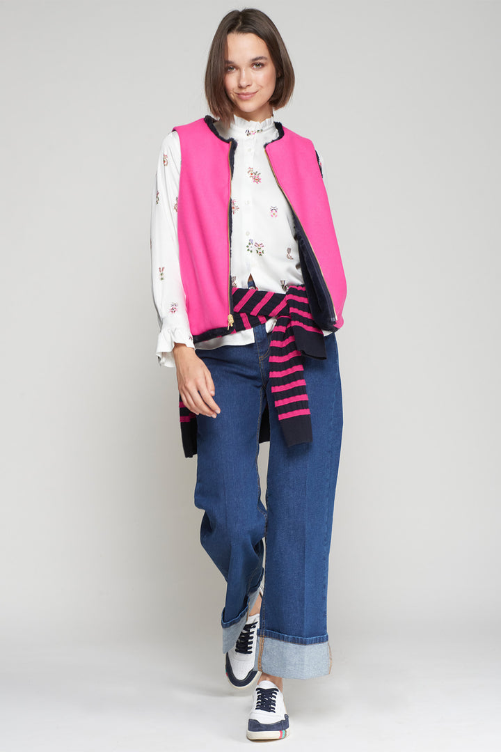 Woman wearing a pink vest, white shirt, blue jeans, and striped socks on a plain background