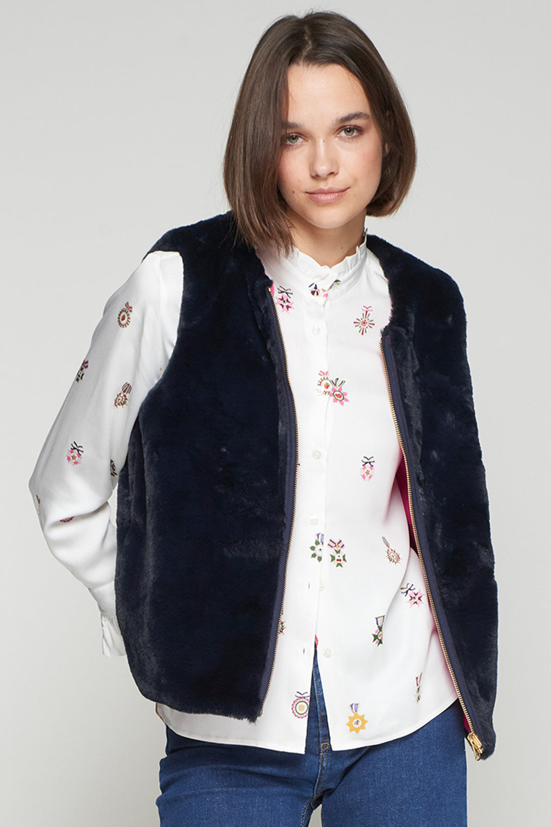 Woman wearing a navy blue vest over a white floral blouse on a plain background