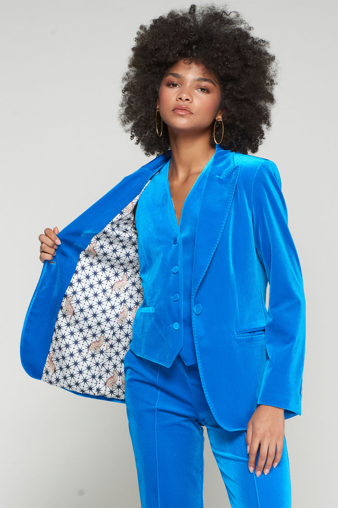 Woman wearing a bright blue suit holding a patterned handbag against a plain background
