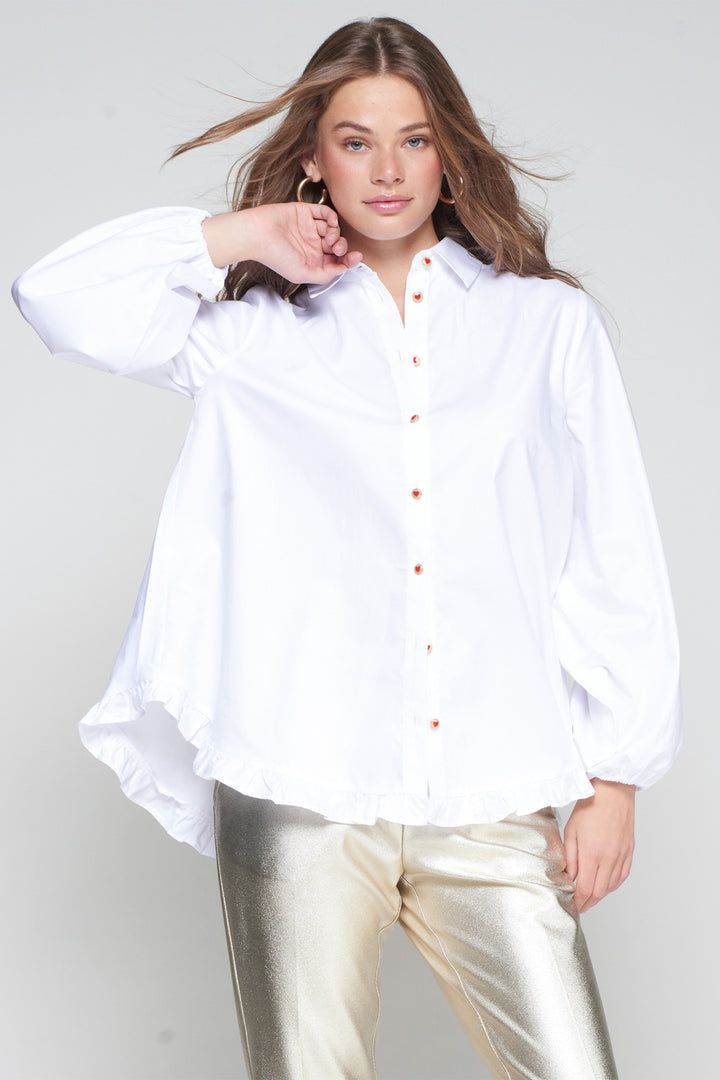 Woman wearing a white button-up shirt and gold pants on a plain background