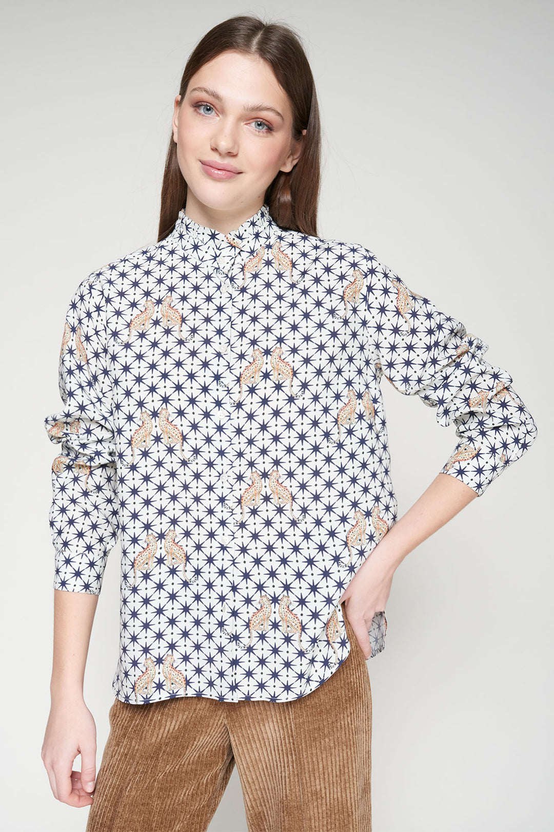 Woman wearing a patterned shirt and brown pants on a white background