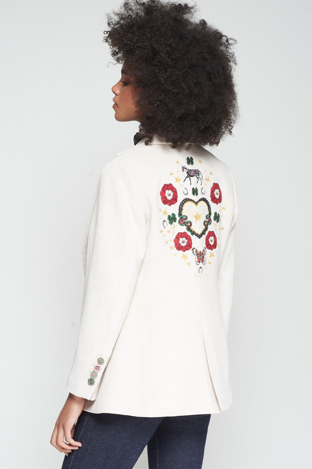 Person wearing a white blazer with floral embroidery on a plain background