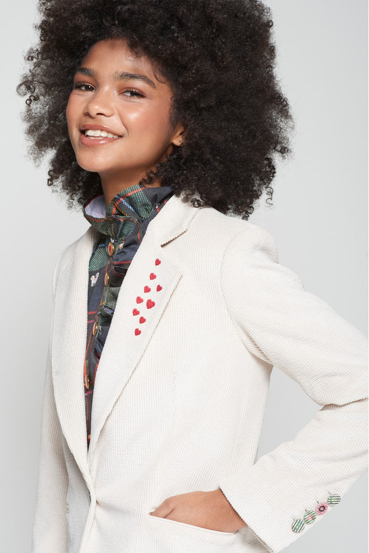 Person wearing a white blazer with red heart patterns on a plain background