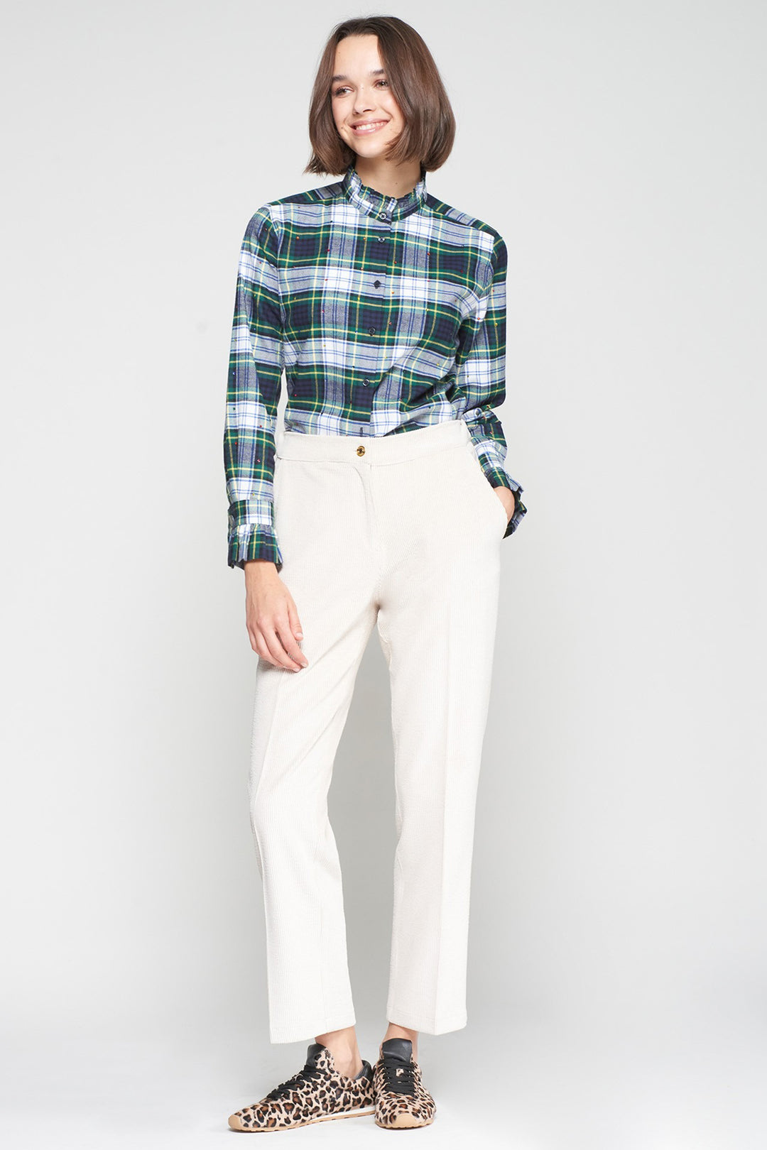 Person wearing a green and blue plaid shirt with white pants on a plain background