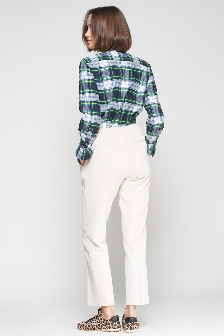 Person wearing a green and blue plaid shirt with white pants on a plain background