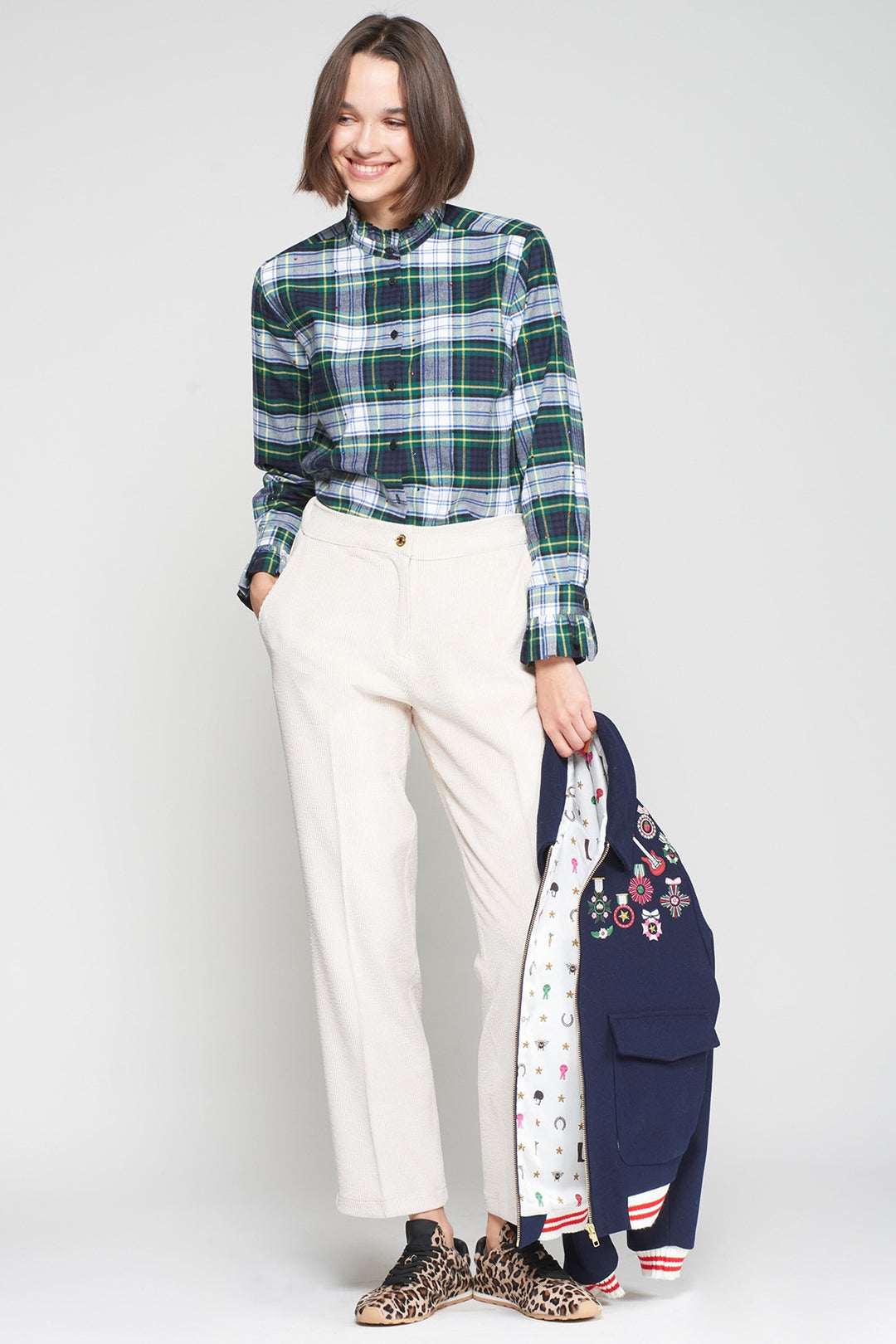Woman wearing a plaid shirt and white pants with a colorful bag on a white background